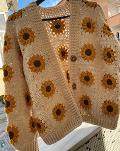 a crocheted sweater with sunflowers is hanging on a clothes rack outside