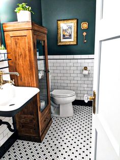 a white toilet sitting next to a wooden cabinet in a bathroom with black and white tiles