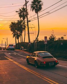 a car is driving down the road at sunset with palm trees in the foreground