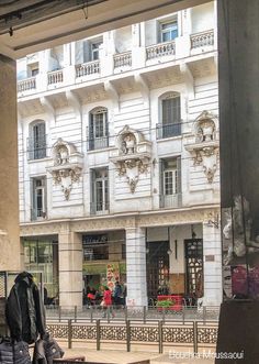 people are sitting on benches in front of a large white building with balconies