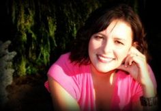 a woman in a pink shirt is smiling for the camera with her hand on her chin