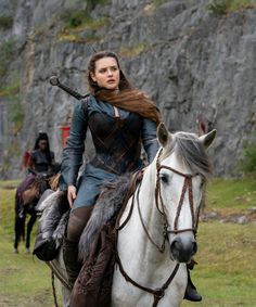 a woman riding on the back of a white horse next to a man in armor