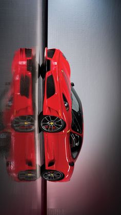 two red sports cars parked next to each other in front of a wall with mirrors