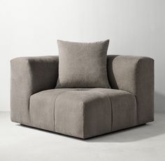 a gray chair sitting on top of a floor next to a white wall with two pillows