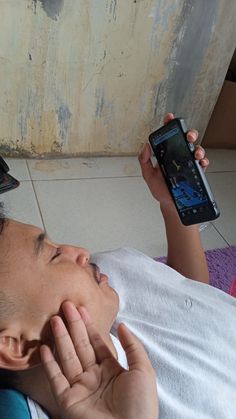 a man laying on the floor while looking at his cell phone and holding it up to his ear