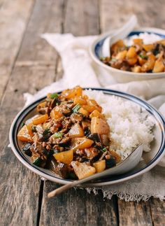 two plates filled with food sitting on top of a wooden table next to white rice