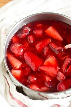 a metal bowl filled with sliced strawberries on top of a white cloth next to a wooden spoon