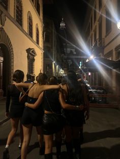 three women in short skirts are standing together on the street at night with their arms around each other