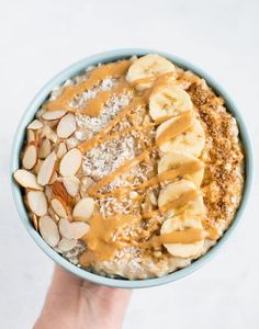 a hand holding a bowl of oatmeal with bananas, almonds and peanut butter