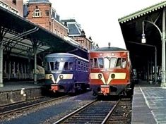 two trains parked next to each other on train tracks in front of a brick building