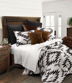 a bed with black and white comforter in a bedroom next to a dresser, lamp and window