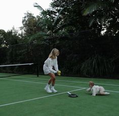 a woman is playing tennis with her dog on the green court, while another dog looks on