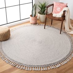 a round rug with tassels on the floor next to a chair and potted plant