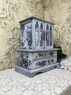 an old fashioned dresser is sitting on a table with a floral wallpaper behind it