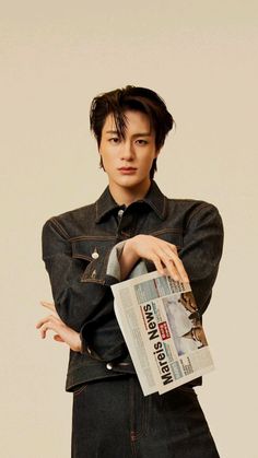 a young man is posing with his arms crossed and looking at the camera while holding a newspaper