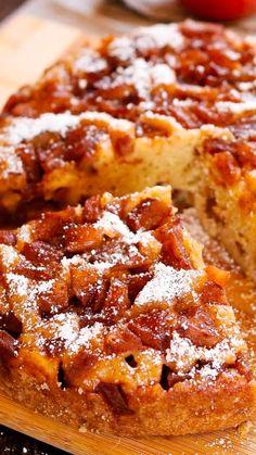 a close up of a cake on a cutting board with powdered sugar and an apple in the background