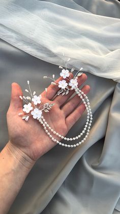 a woman's hand is holding two white flowers and pearls on a silver satin background