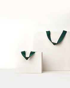 two white bags with green handles are sitting next to each other on a table in front of a white wall