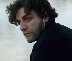 a close up of a person near water with a black jacket on and one eye open