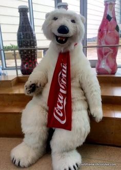 a large white polar bear with a coca cola ribbon around it's neck sitting on some steps