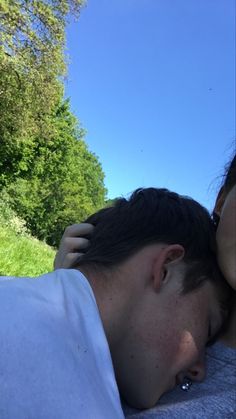 a man and woman laying on top of each other in the grass with trees behind them