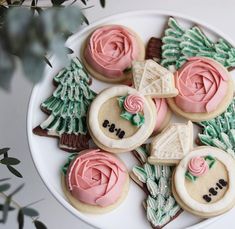 decorated cookies on a plate with pink frosting and green leaves around the edges, sitting on a table