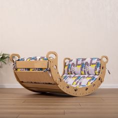 a child's rocking chair made out of wood and fabric, sitting on the floor next to a potted plant