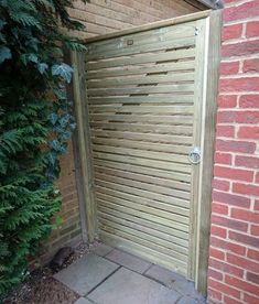 an open wooden gate in front of a brick wall and green plants next to it