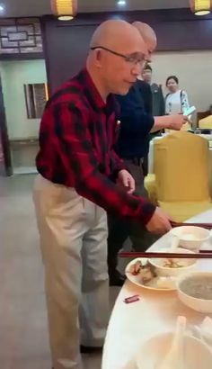 an older man standing in front of a table filled with plates of food and chopsticks