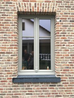 a man standing in front of a window next to a brick building with white trim