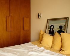 a bed with yellow pillows and two pictures on the headboard, in front of a wooden door