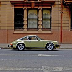 an old green porsche parked on the side of the road in front of a building