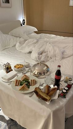 a table with food and drinks on it in a hotel room or suite, next to an unmade bed