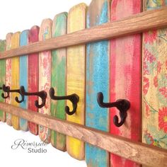 a wooden wall mounted coat rack with three hooks on it and colorful painted wood boards behind it