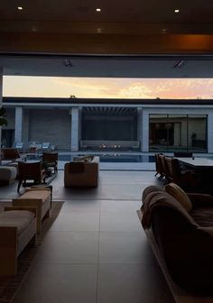 a living room with couches and tables in front of a large open window at sunset