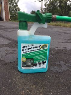 a bottle of liquid sitting on the ground next to a green hose and spigot