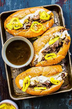 two sandwiches with meat, cheese and peppers on a tray next to a dipping sauce