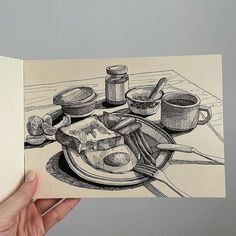 a hand holding up a drawing of food on a plate with utensils and saucers