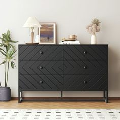 a black dresser sitting on top of a wooden floor next to a potted plant