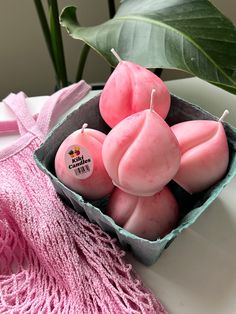 some pink candles are sitting in a box on a table next to a green plant