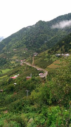 a scenic view of a small town nestled on a mountain side with lush green trees and mountains in the background