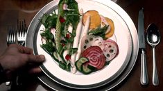 a white plate topped with lots of veggies and meat next to silverware