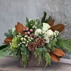 a vase filled with flowers and greenery sitting on top of a wooden table next to a wall