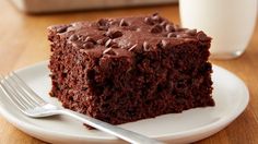 a piece of chocolate cake sitting on top of a white plate next to a glass of milk