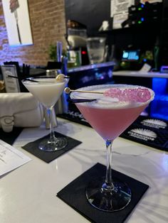 two martinis sitting on top of a table next to each other in front of a bar