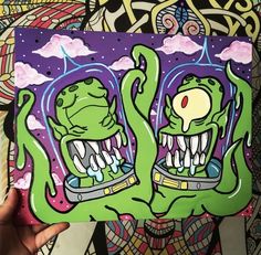 someone holding up a piece of art that looks like two green monsters with their mouths open