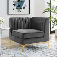 a gray velvet chair with gold legs in a living room next to a table and potted plant