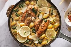 a pan filled with chicken, potatoes and lemons on top of a white table