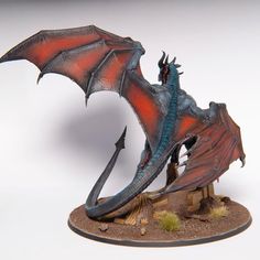 a red and blue dragon figurine sitting on top of a wooden base with an arrow in it's mouth