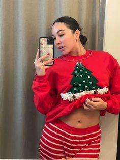 a woman taking a selfie in front of a christmas tree sweatshirt and striped shorts